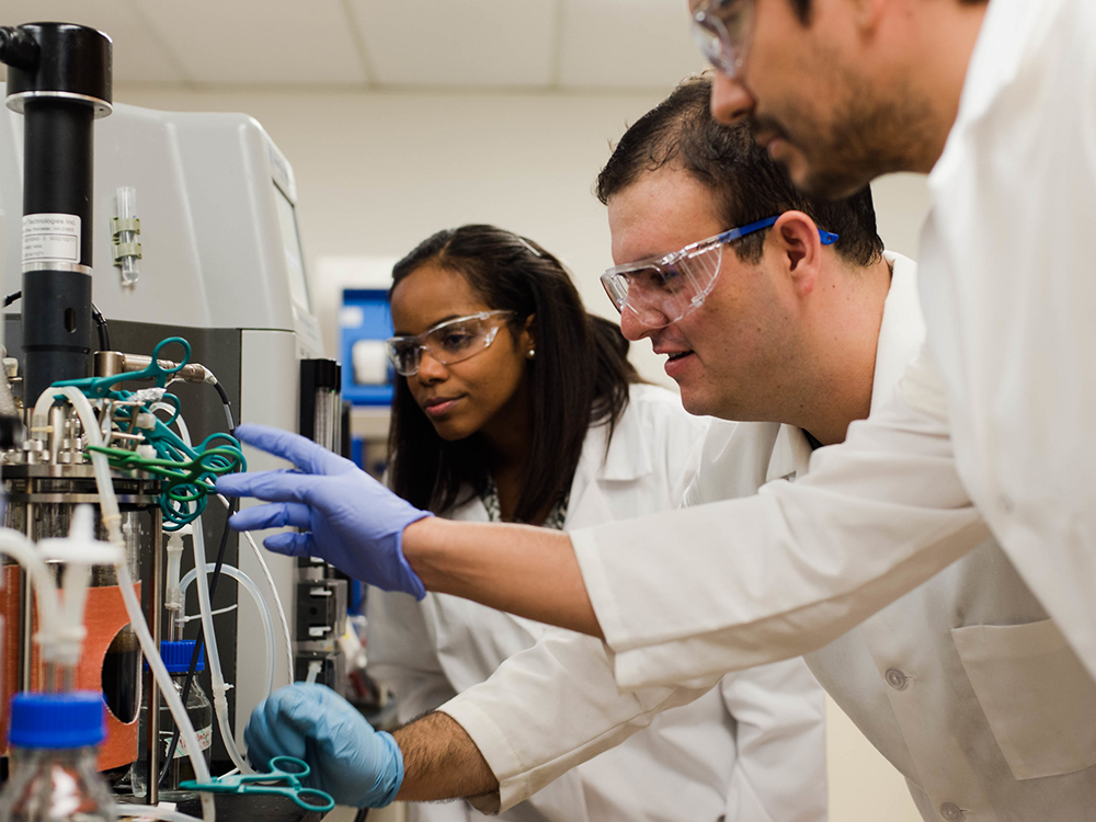 three people in lab coats looking at beaker