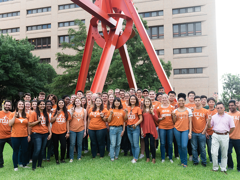 group of students in orange shirts in front of clock knot scultpure