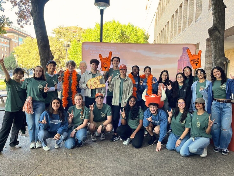 Student volunteers gather in front of a backdrop at the annual McKetta Tailgate. 